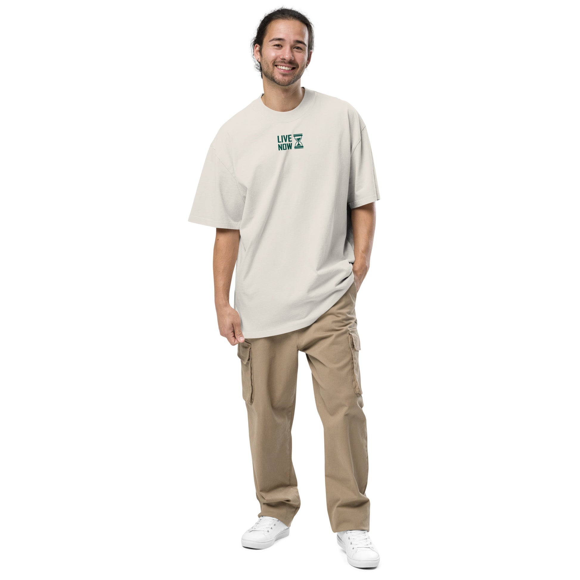 Jeune homme souriant portant un t-shirt oversize beige délavé avec inscription 'LIVE NOW' et pantalon cargo beige